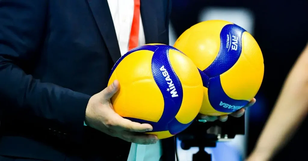 How to Keep Score in Volleyball: A referee holding two Volleyballs in his hand